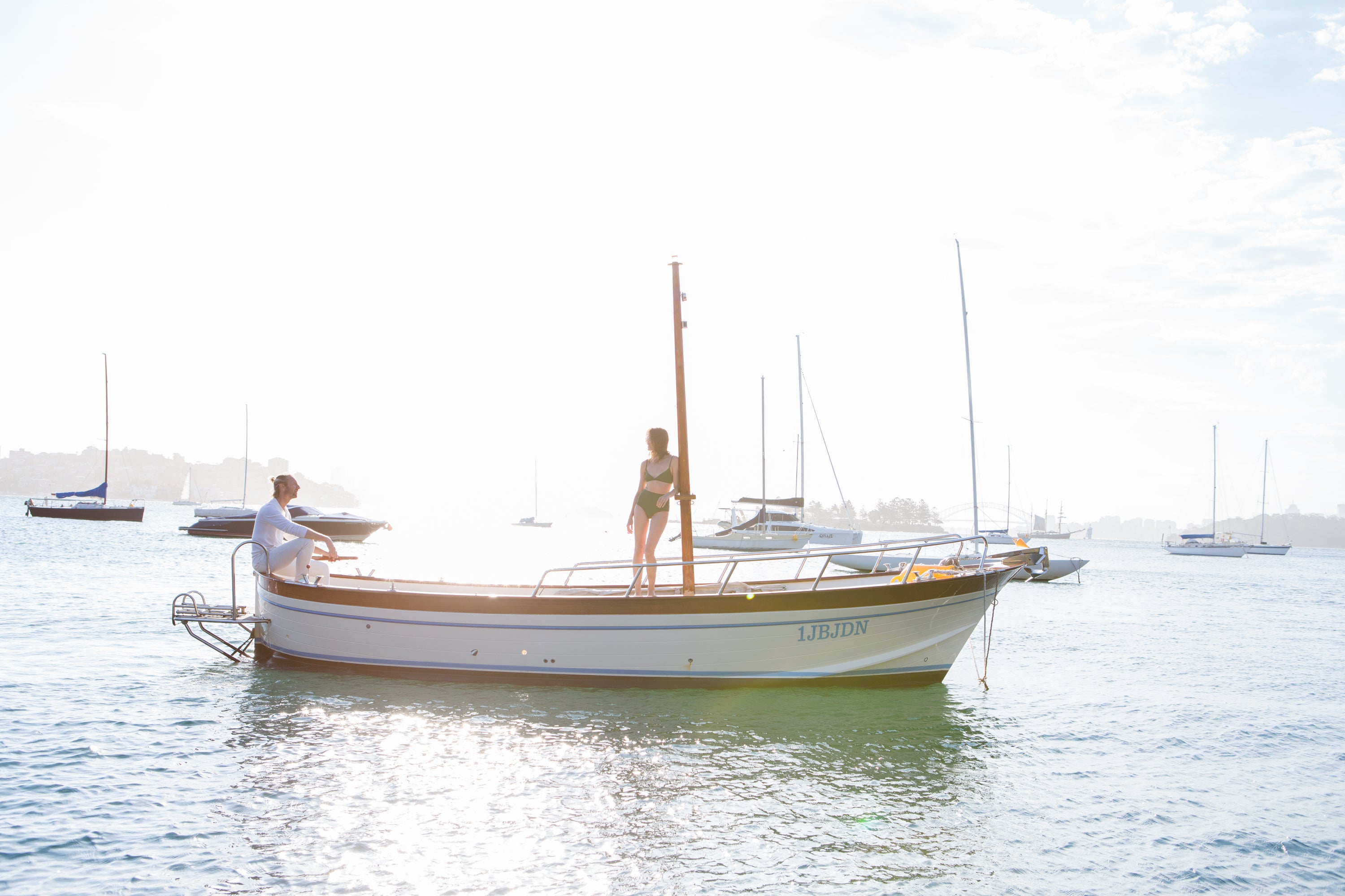 Two people on a small boat in a harbor with other boats in the background — editorial photography by Carla Coulson