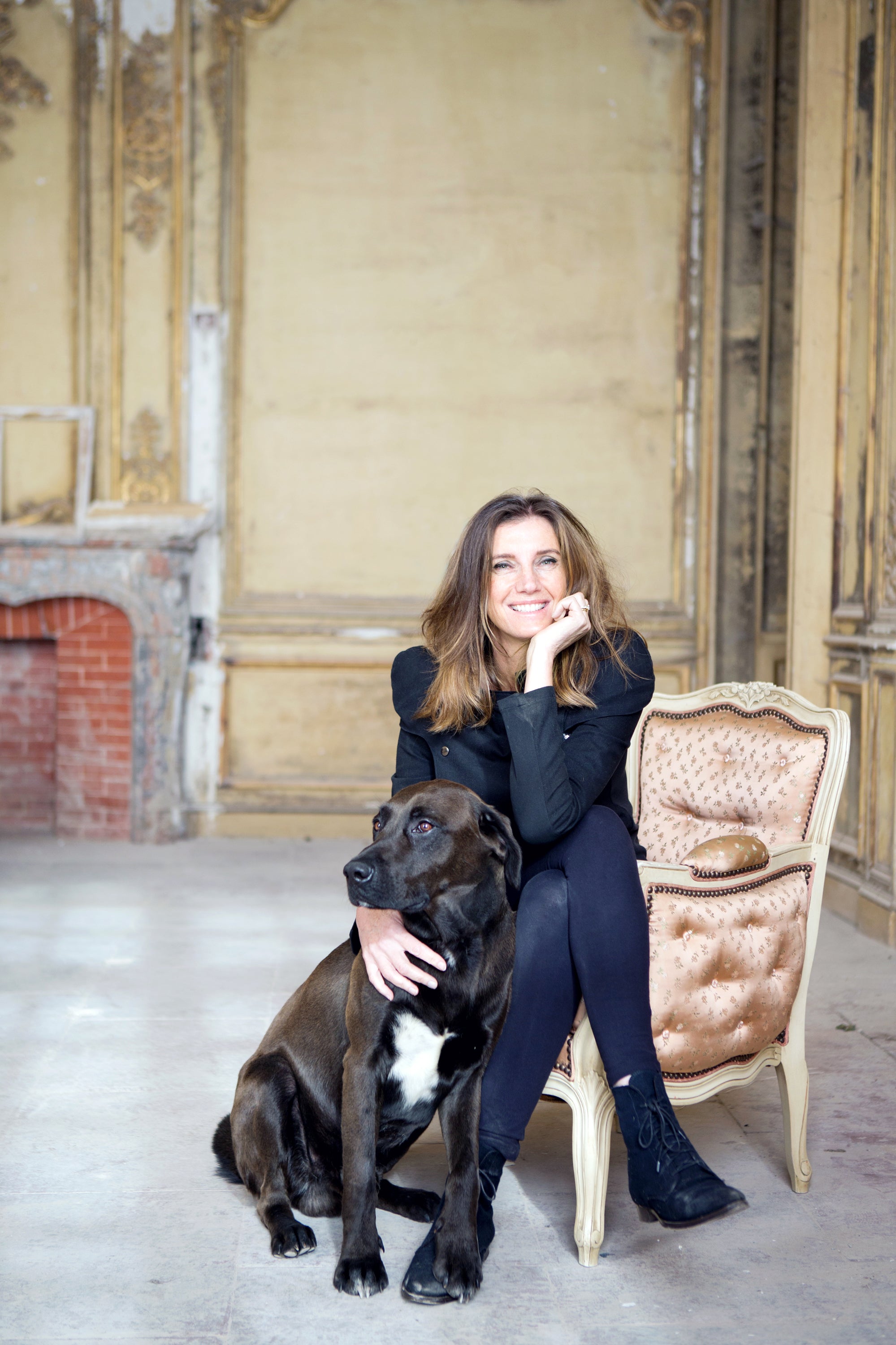 Woman sitting on a chair with a large dog in an elegant room in French chataeu with warm lighting — editorial property photography by Carla Coulson