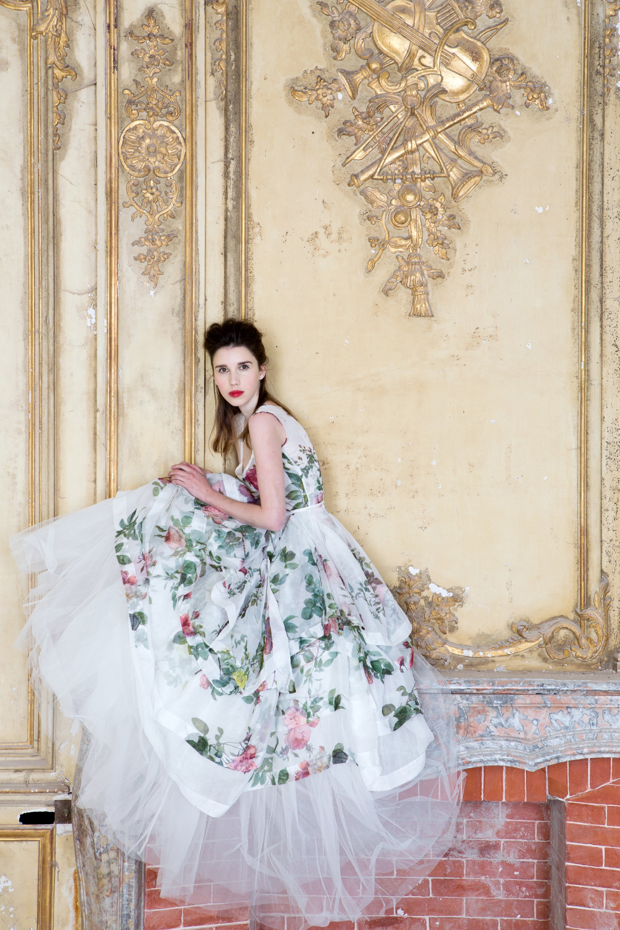 Woman in a floral dress standing in an ornate room with gold wall decorations — editorial photography by Carla Coulson
