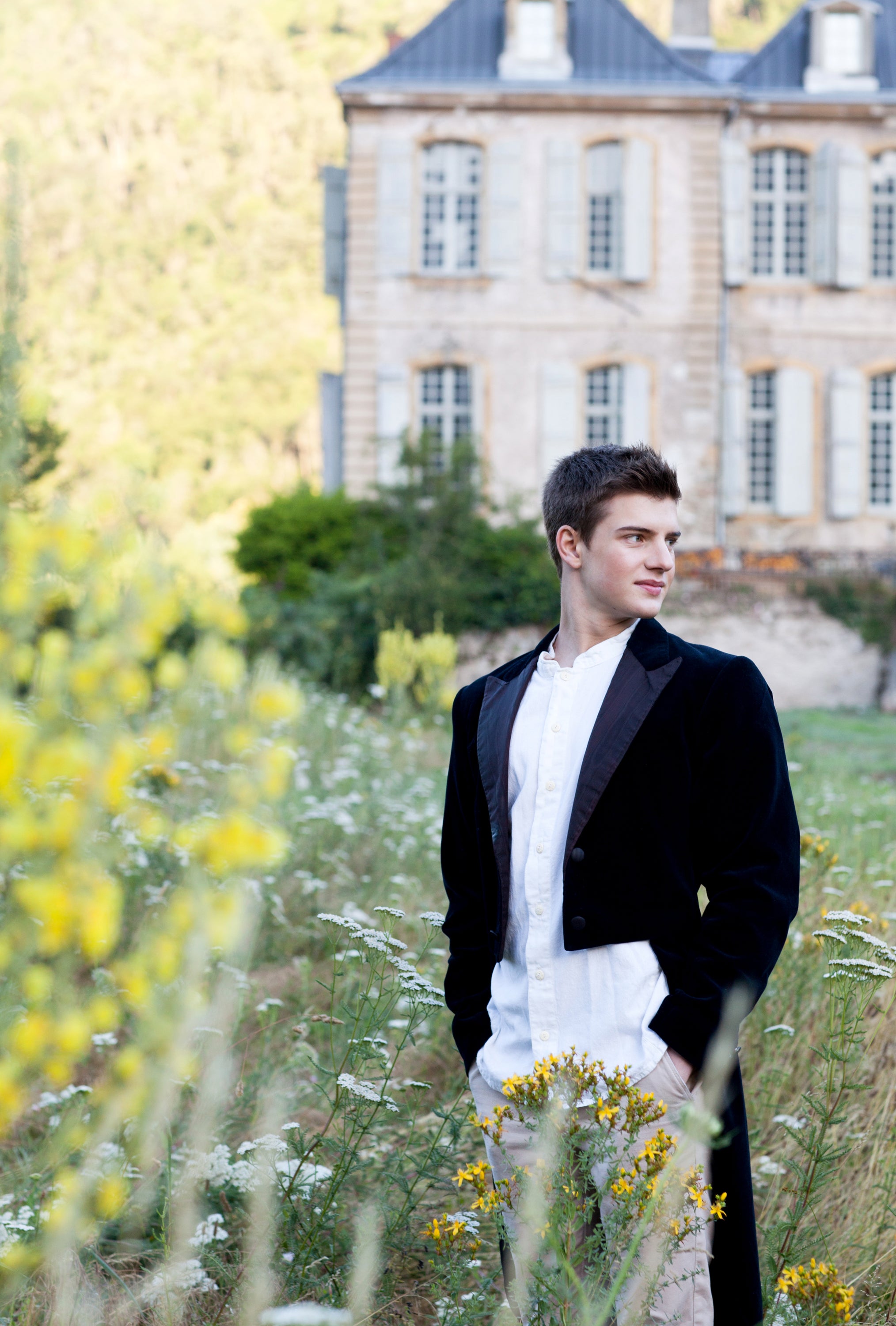 Man in formal attire standing in a field with a French chateau in the background — editorial photography by Carla Coulson