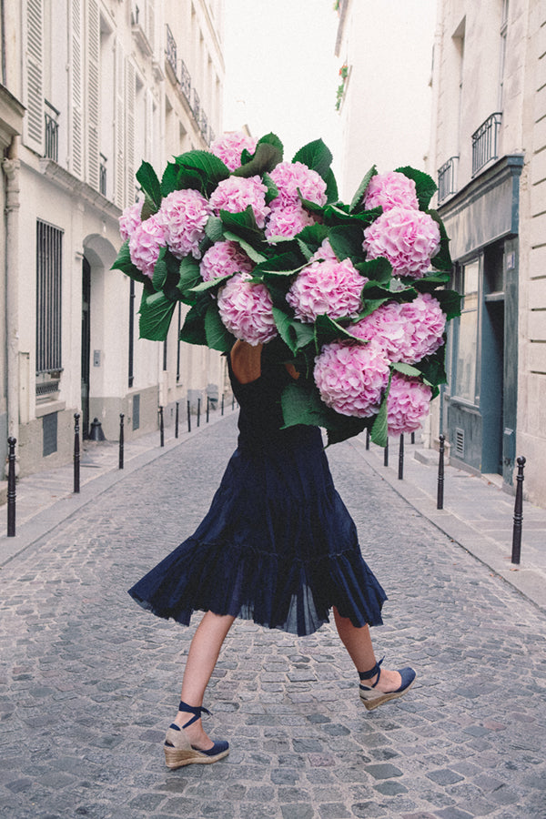 Free and Fearless is a photo of a girl in Paris in St Germain des Prés holding a giant bouquet of pink hydrangeas and is part of a limited edition series named Young Girl in Bloom by photographer Carla Coulson celebrating women loving and believing in themselves and building their self esteem by trusting their intuition.