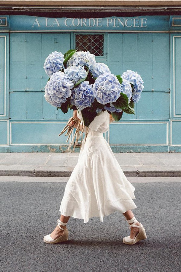 Out Of The Blue is a photo of a girl in Paris in St Germain des Prés holding the biggest bunch of baby blue hydrangeas and is part of a limited edition series named Young Girl in Bloom by photographer Carla Coulson celebrating women loving and believing in themselves and building their self esteem by trusting their intuition.