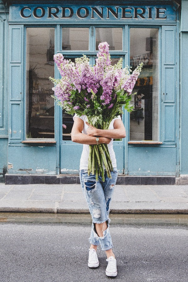 I Saw You Standing There is a photo of a girl in Paris in Le Marais holding a bouquet of purple delphiniums and is part of a limited edition series named Young Girl in Bloom by photographer Carla Coulson celebrating women loving and believing in themselves and building their self esteem by trusting their intuition.